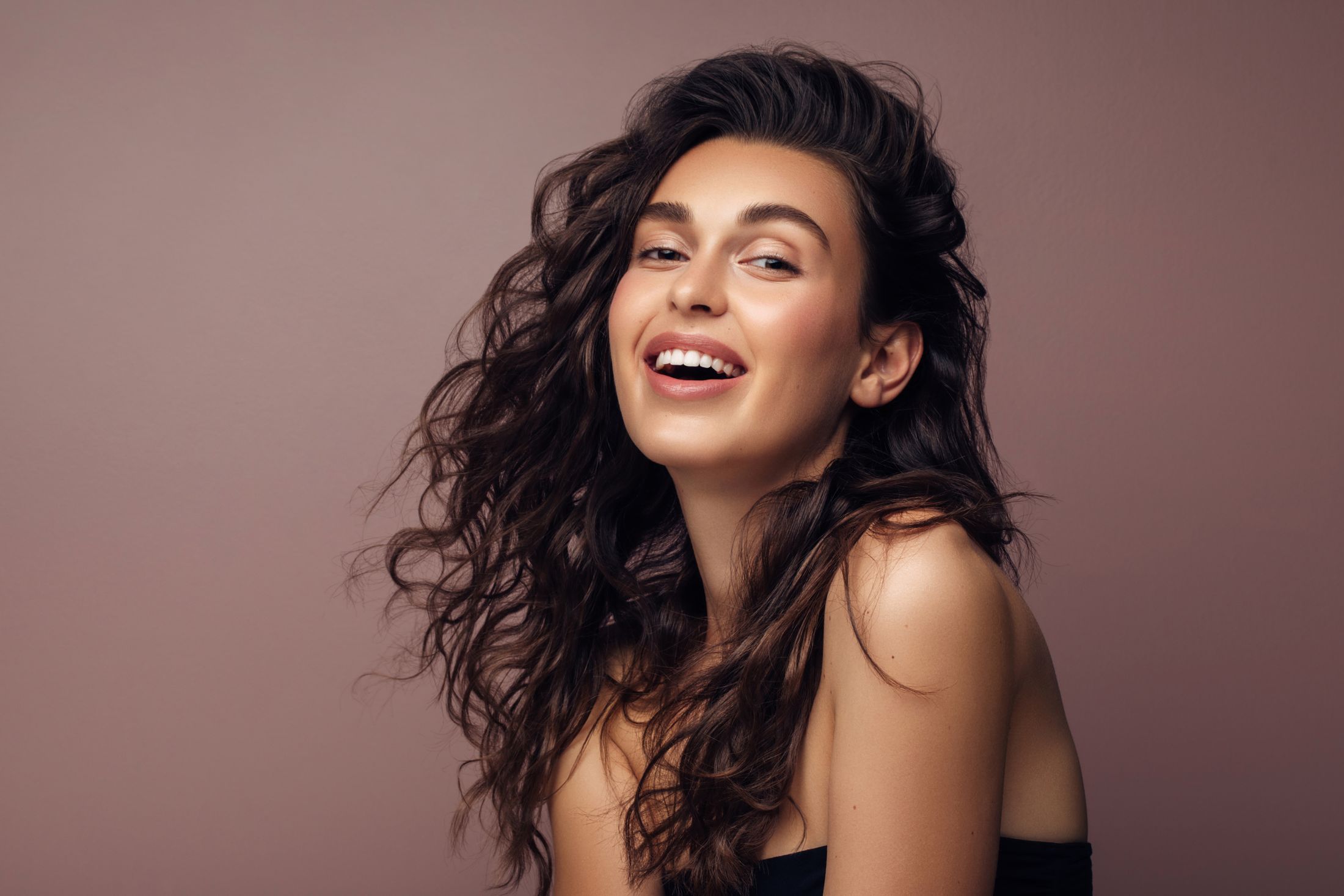 Smiling woman with curly hair on neutral background.