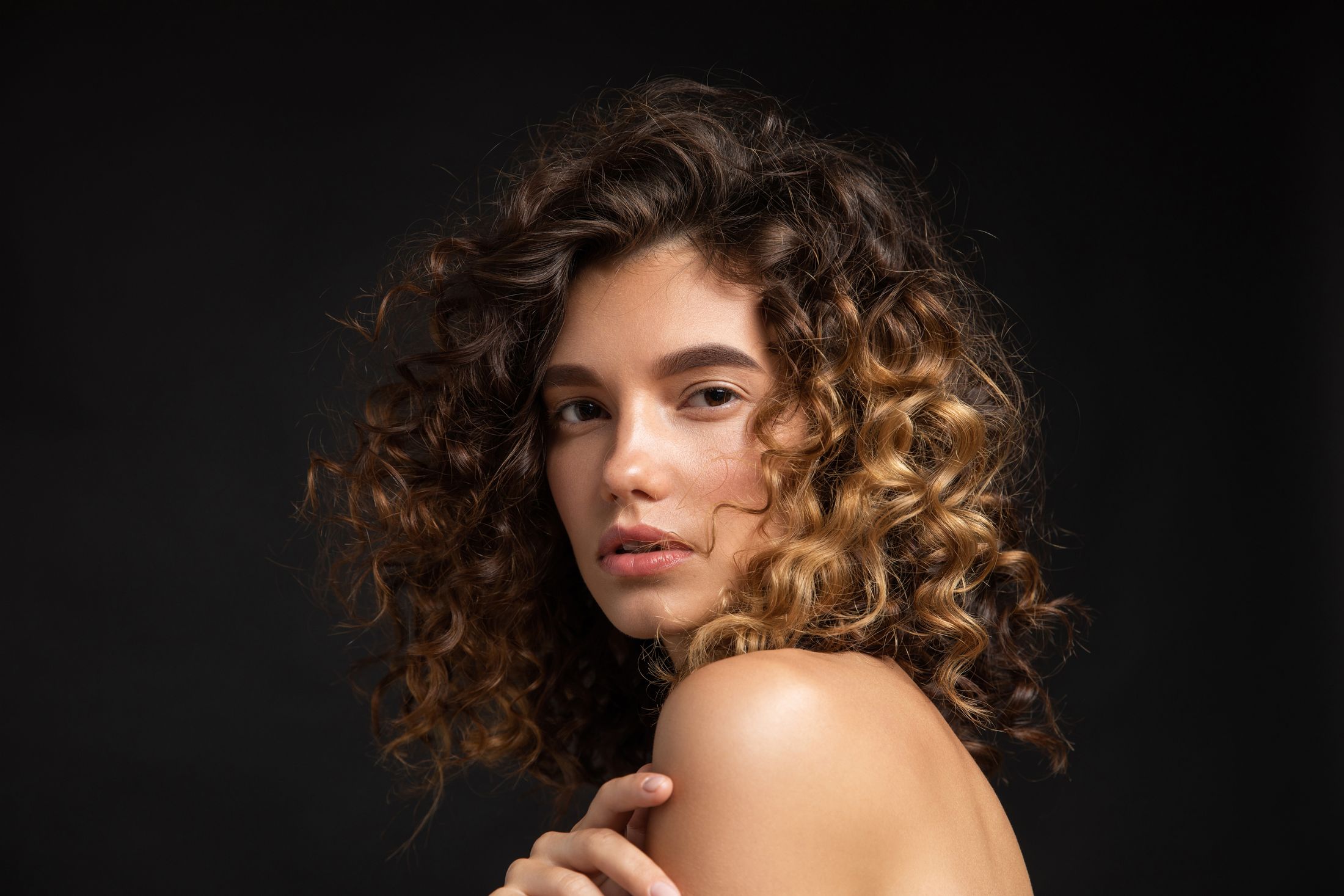 Person with curly hair on black background.